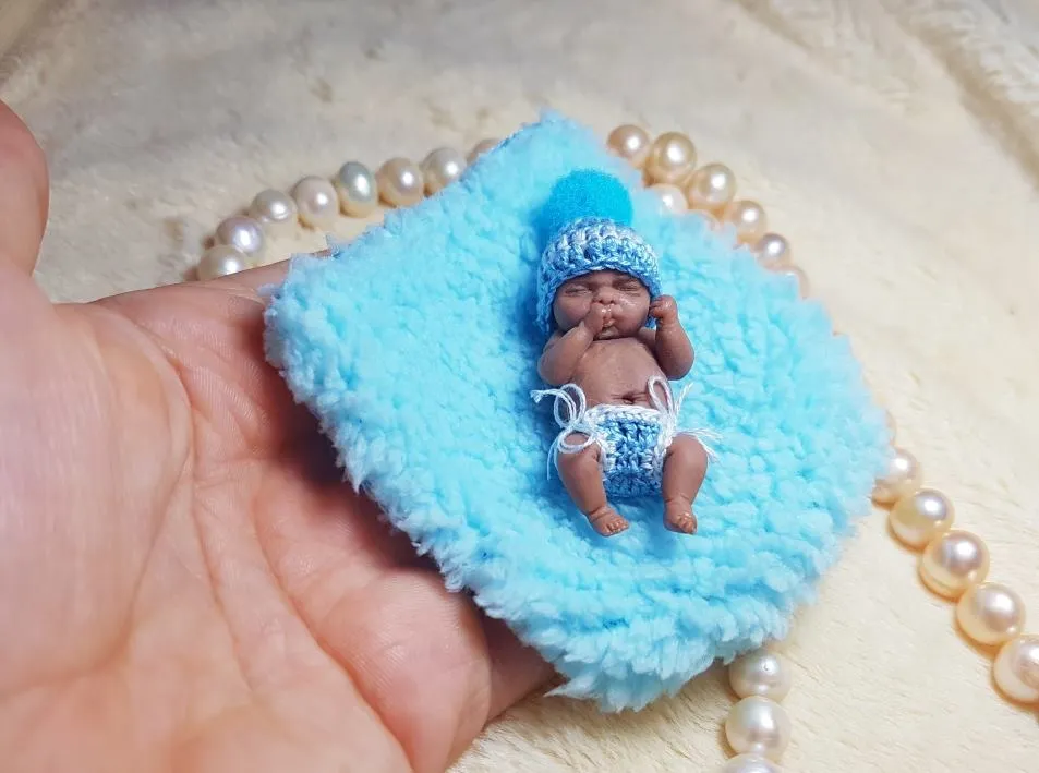 Adorable OOAK miniature baby doll on fluffy blue crocheted pillow wearing a matching blue bonnet, displayed with pearl beads - by Mini Baby Dolls