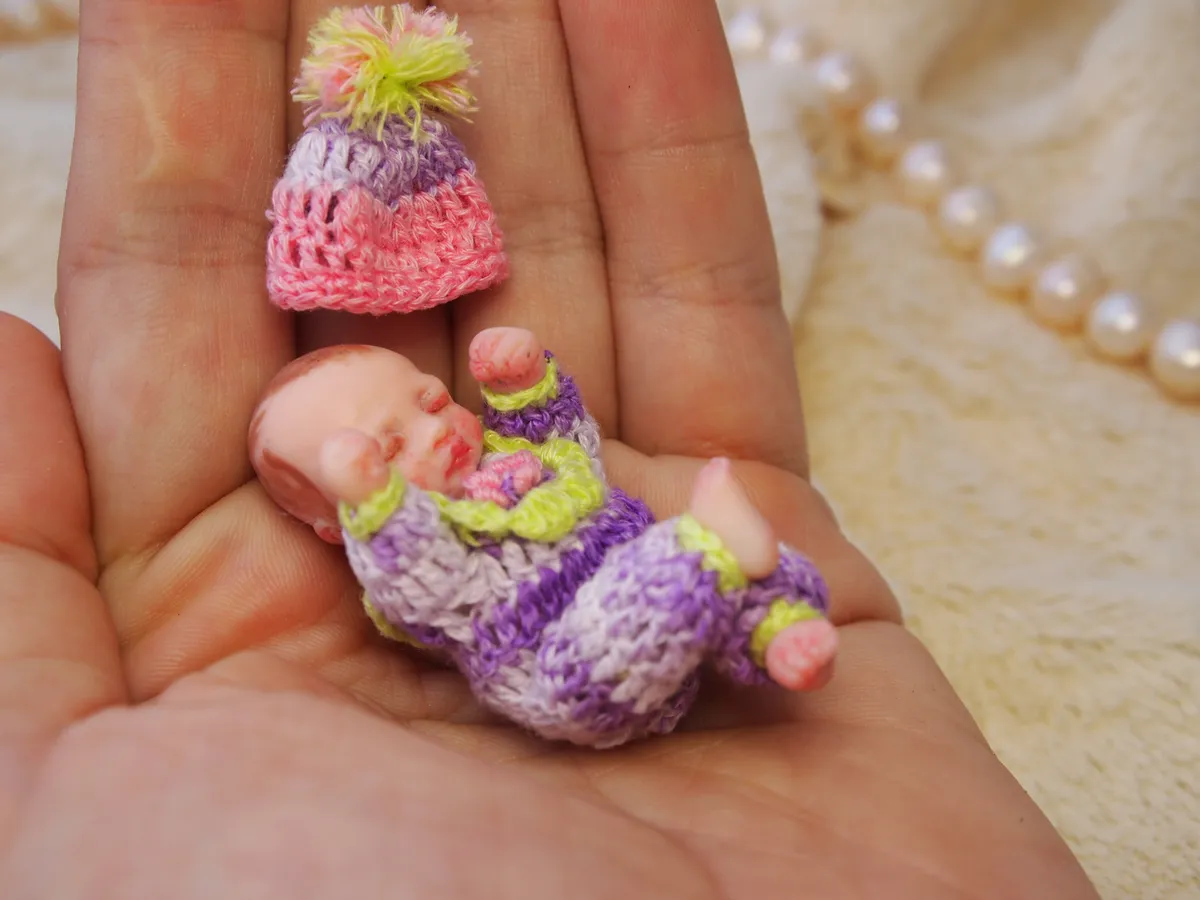 Handcrafted polymer clay miniature baby doll wearing a colorful handmade winter pom-pom hat in pink, yellow and green hues - by Mini Baby Dolls