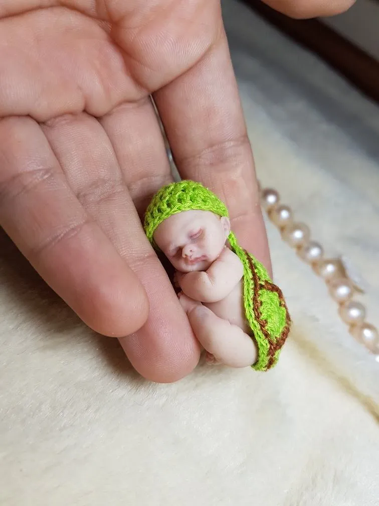 Whimsical OOAK miniature baby doll in green crocheted pea pod outfit with matching bonnet, displayed in palm with pearl beads - by Mini Baby Dolls