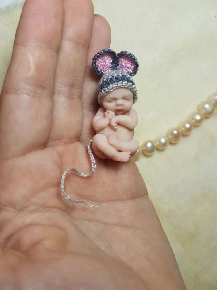Adorable OOAK miniature baby doll wearing a grey crocheted mouse-ear hat with pink inner ears and bow, sleeping peacefully in palm - by Mini Baby Dolls
