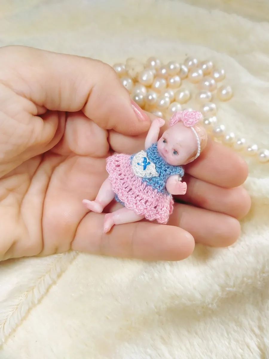 Sweet OOAK miniature baby doll in pink and blue crocheted dress with matching pink bow headband, displayed in palm with pearl beads - by Mini Baby Dolls