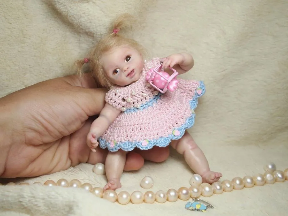 Detailed OOAK miniature baby doll with blonde hair, wearing a pink crocheted dress with blue trim, holding a tiny bottle - by Mini Baby Dolls