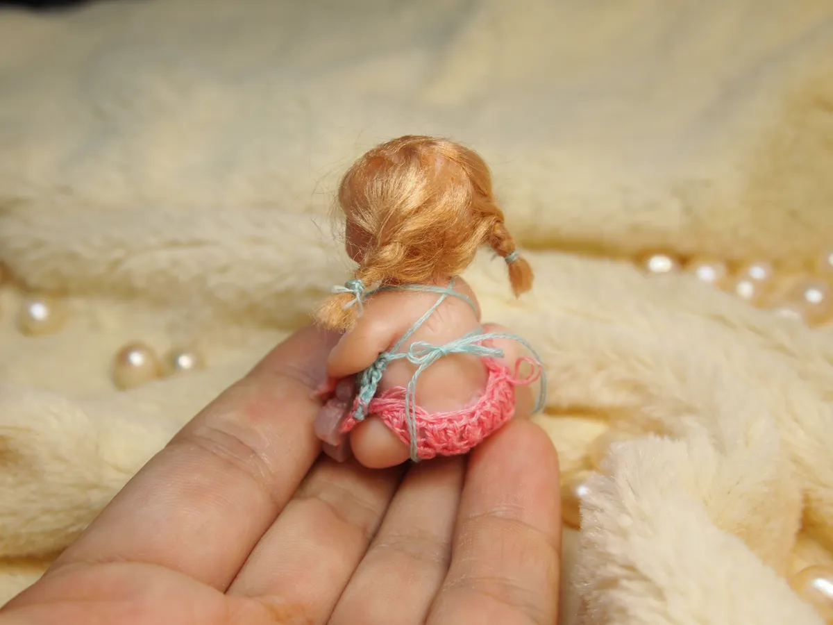 OOAK miniature toddler doll with blonde hair in pink crocheted bikini, sitting view from behind with pearl beads - by Mini Baby Dolls