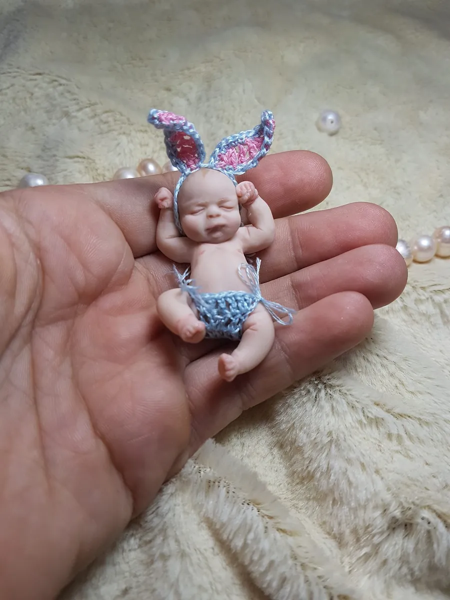 Sweet OOAK miniature baby doll in blue crocheted bunny ears and matching diaper, happily posed in palm with pearl beads - by Mini Baby Dolls