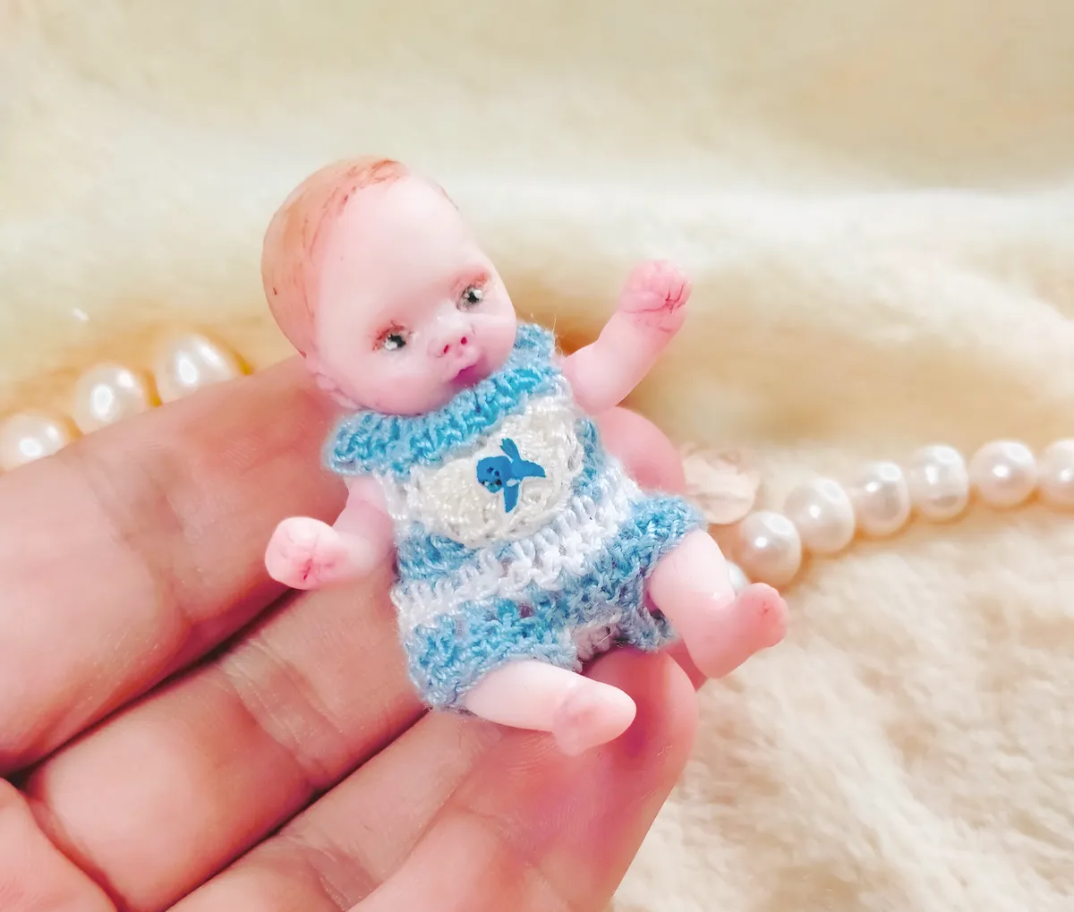 Cheerful OOAK miniature baby doll in blue and white striped crocheted romper with tiny bow, waving hand, displayed with pearl beads - by Mini Baby Dolls