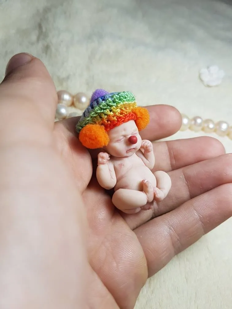 Playful OOAK miniature clown baby doll in rainbow crocheted hat with colorful pom poms, held gently in palm with pearl beads - by Mini Baby Dolls
