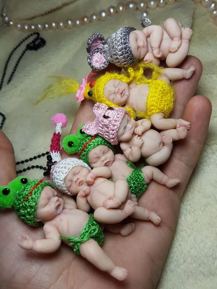 Colorful collection of OOAK miniature baby dolls in palm - various costumes including frogs, mermaids, and colorful outfits in yellow, pink, and green - by Mini Baby Dolls