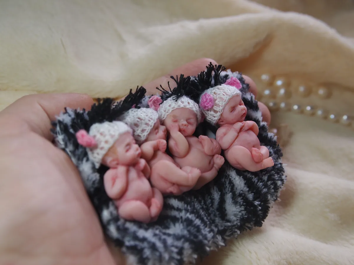 Multiple sleeping OOAK miniature baby dolls cuddled together in dark knitted carrier basket held in palm - by Mini Baby Dolls