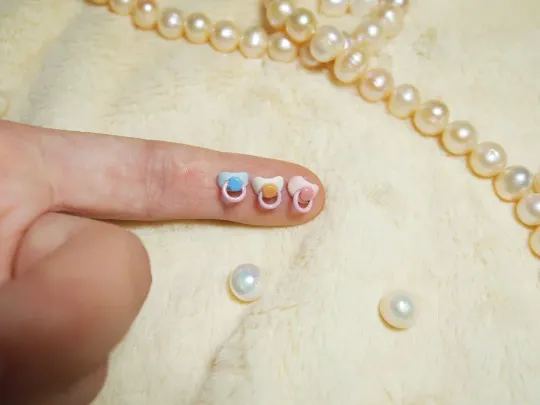 Scale demonstration showing miniature doll fingernails compared to three tiny pearl-sized spheres on fingertip - by Mini Baby Dolls