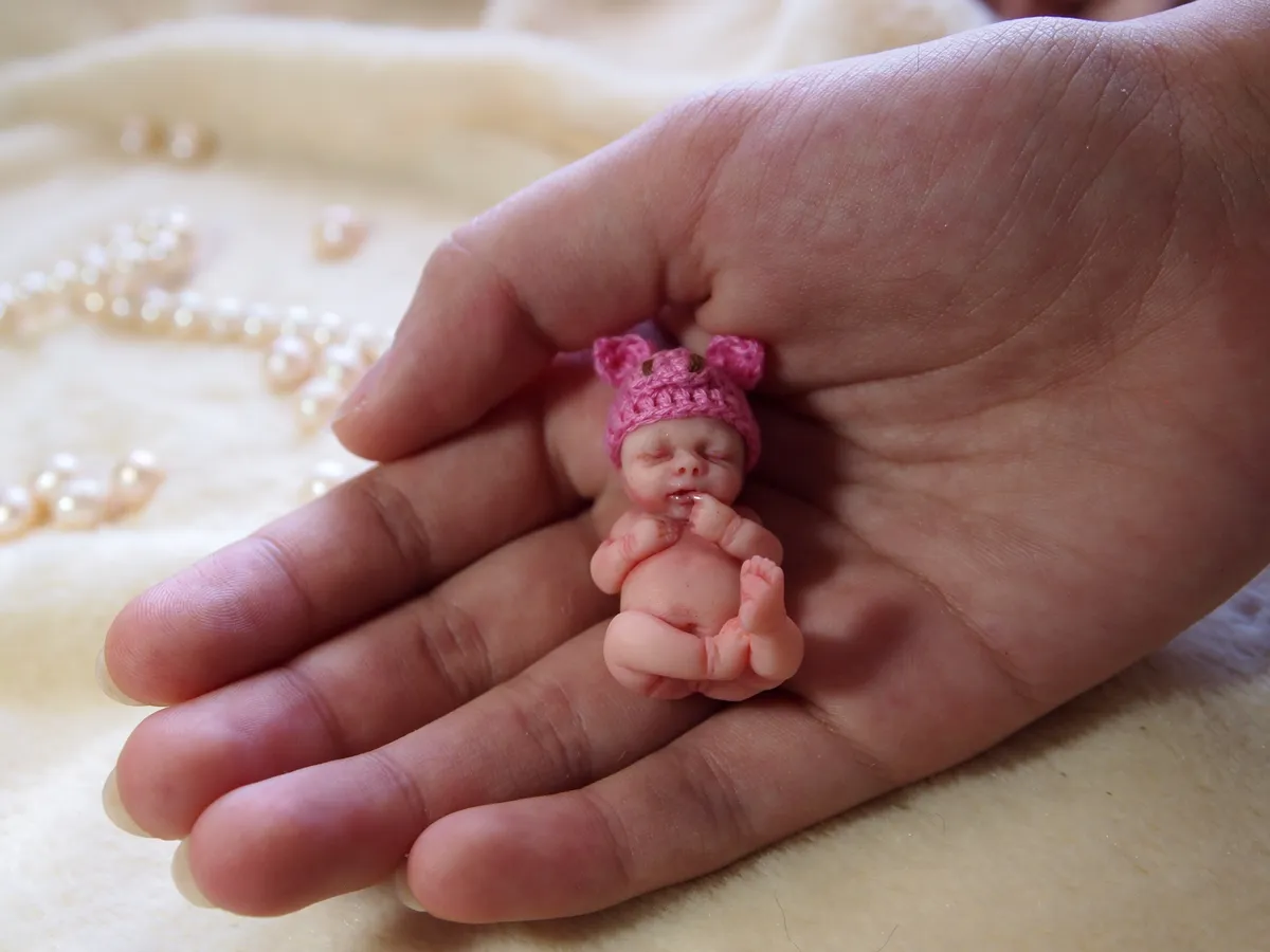 Sleeping OOAK miniature baby doll in pink teddy bear costume with ears, cradled in palm - by Mini Baby Dolls