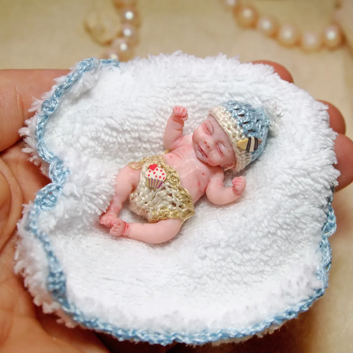 Regal OOAK miniature baby doll wearing a delicate gold crown and lace bodysuit, resting on a handmade white crocheted blanket with blue trim - by Mini Baby Dolls