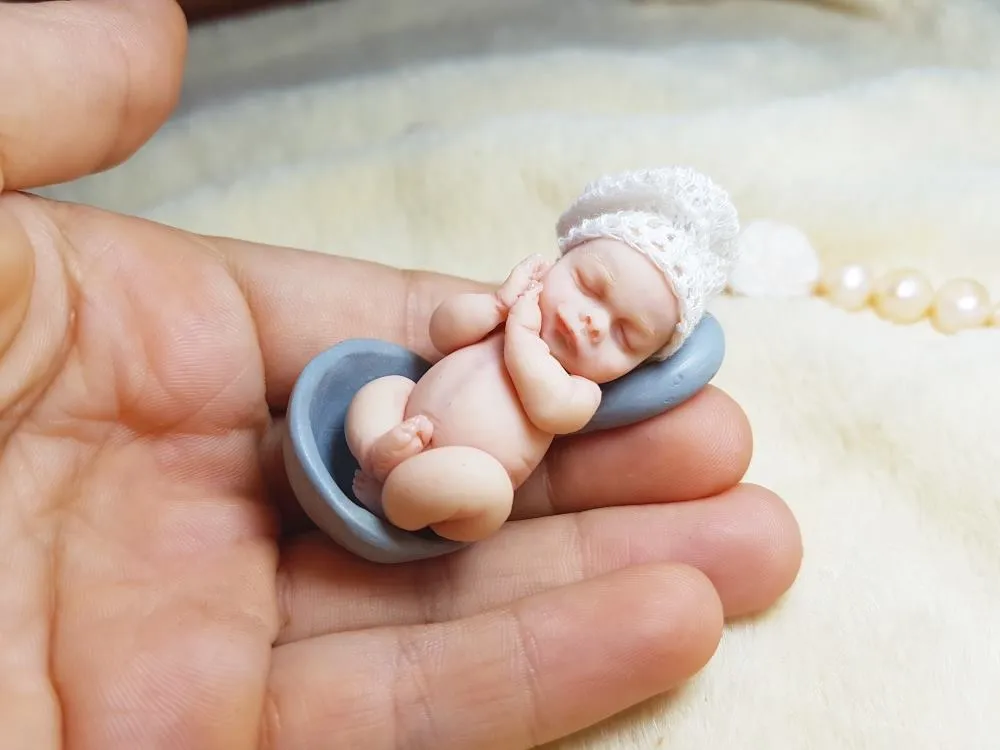 Sleeping OOAK miniature baby doll in blue crocheted outfit with white pompom detail, held in palm with pearl beads - by Mini Baby Dolls