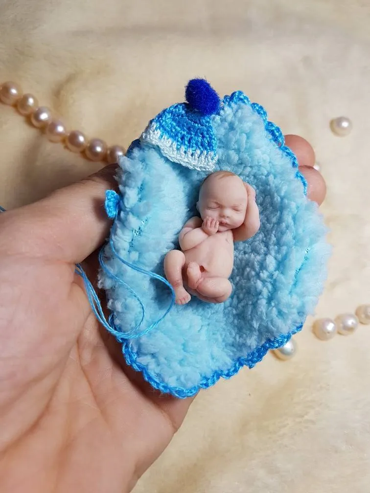 Peaceful sleeping OOAK miniature baby doll on fluffy blue crocheted blanket wearing a matching blue pom pom hat, held gently in hands - by Mini Baby Dolls