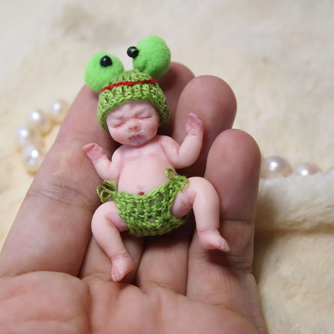 Adorable sleeping OOAK miniature baby doll in handmade green crocheted frog costume with big googly eyes, held gently in palm - by Mini Baby Dolls