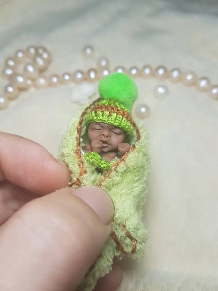 Sleeping OOAK miniature baby doll on yellow-green fuzzy blanket wearing a green striped crocheted hat with bright green pom pom - by Mini Baby Dolls
