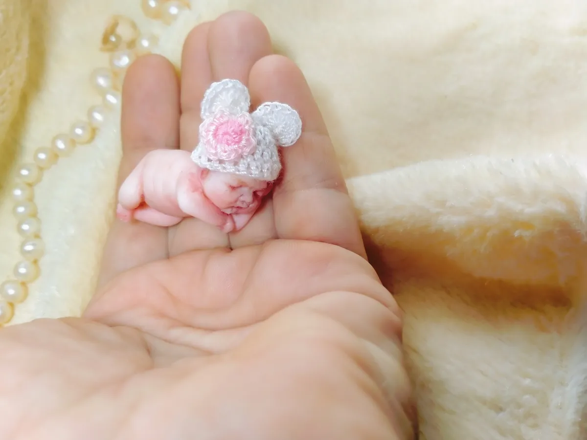 Close-up of sleeping OOAK miniature baby doll in grey crocheted mouse hat with pink and white pom poms - by Mini Baby Dolls