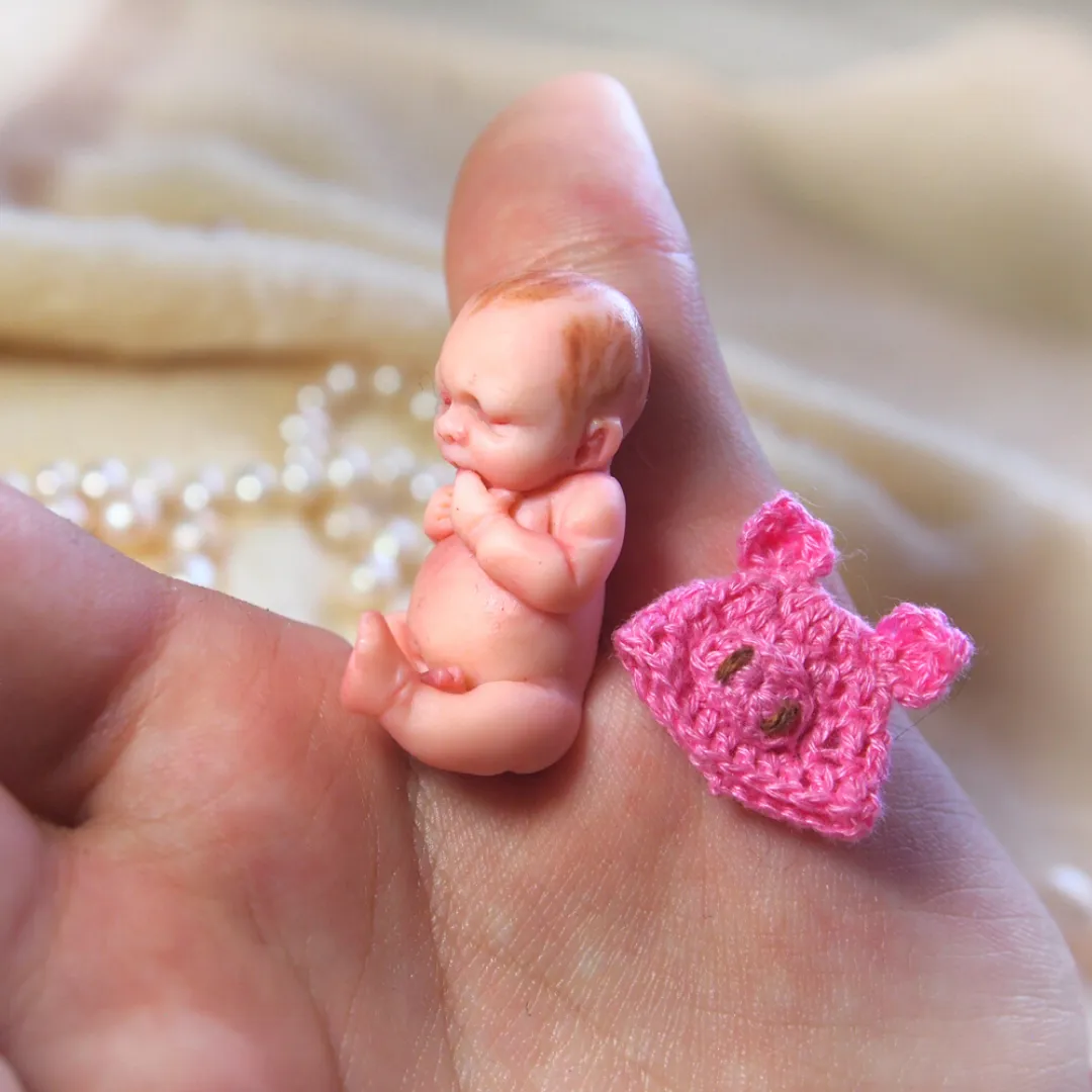 Sleeping OOAK polymer clay miniature baby doll with a tiny handmade pink crocheted teddy bear companion, displayed on soft fabric - by Mini Baby Dolls