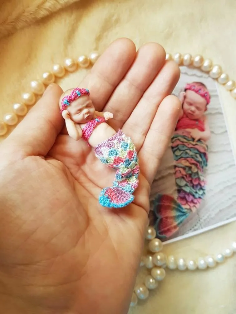 Three adorable OOAK miniature mermaid baby dolls in colorful crocheted mermaid tail costumes - pink, rainbow, and teal - displayed together in palm with pearl beads - by Mini Baby Dolls