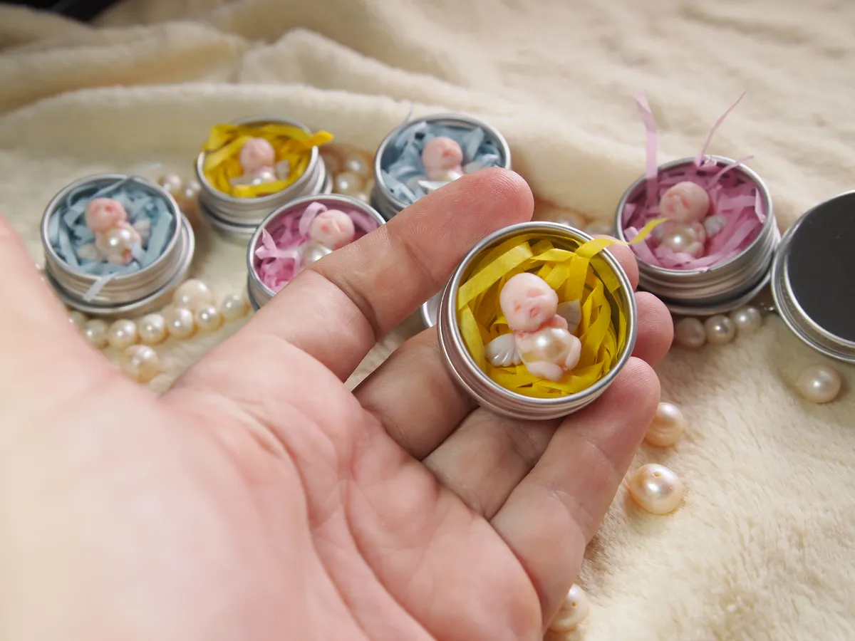 Tiny OOAK miniature baby dolls displayed in small tin containers with decorative bedding, held in palm - by Mini Baby Dolls
