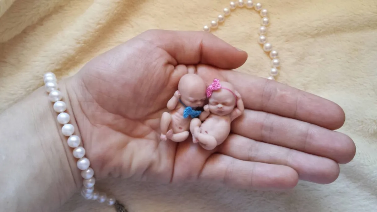 Two tiny OOAK miniature African American baby dolls cuddling together in palm, displayed with pearl beads - by Mini Baby Dolls