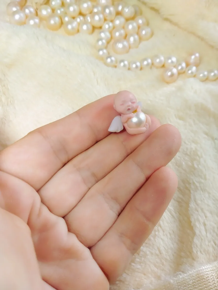 Ultra tiny OOAK miniature baby doll holding oversized pearl bead, displayed in palm with scattered pearls - by Mini Baby Dolls