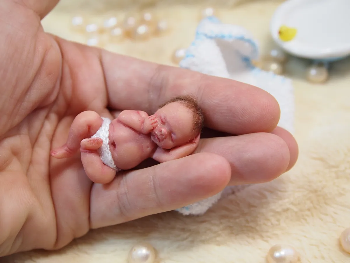 Tiny OOAK miniature baby doll with small white blanket, displayed in palm with soft backdrop - by Mini Baby Dolls