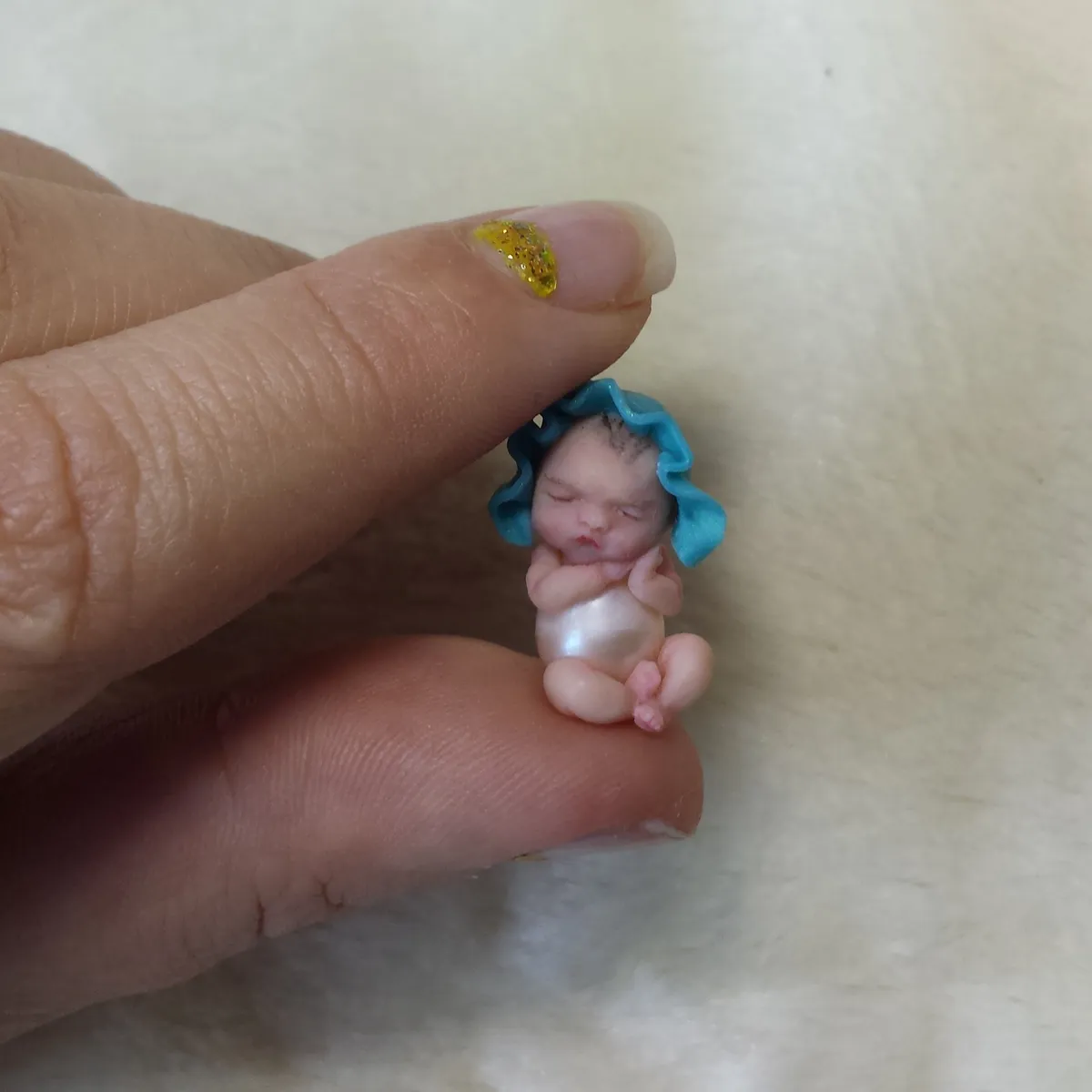 Ultra tiny OOAK miniature mermaid baby doll with blue crocheted tail, held between sparkly manicured fingers for scale - by Mini Baby Dolls