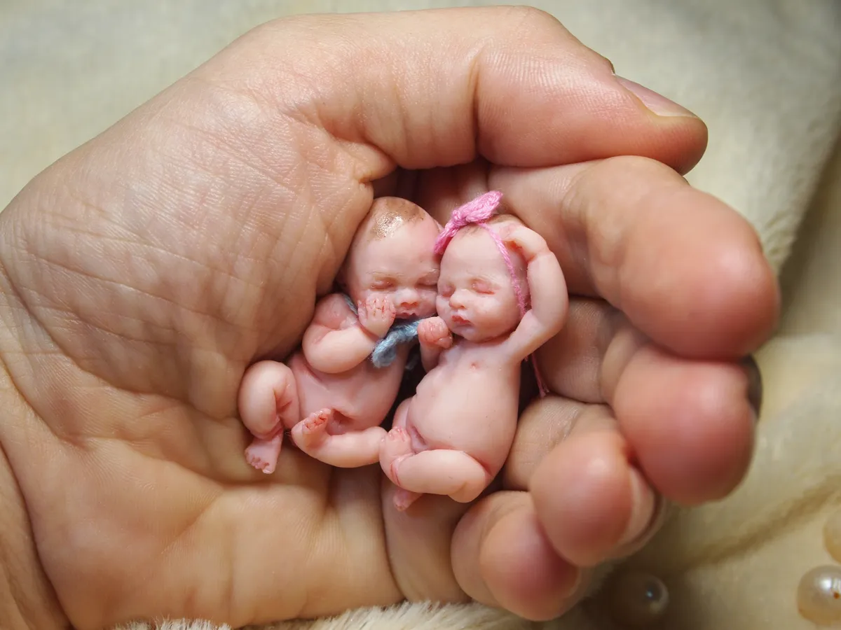 Pair of sleeping OOAK miniature twin baby dolls in pink and blue crocheted outfits, cradled together in palm showing their tiny realistic scale - by Mini Baby Dolls