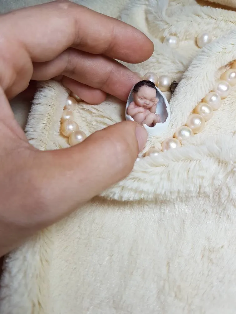 Ultra-miniature OOAK baby doll displayed inside a tiny oval cameo or locket, held between fingers to show incredibly small scale - by Mini Baby Dolls