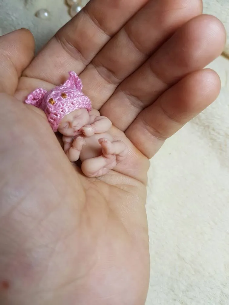 Ultra-tiny OOAK miniature baby doll in delicate pink crocheted outfit, held gently in palm showcasing incredible miniature scale - by Mini Baby Dolls