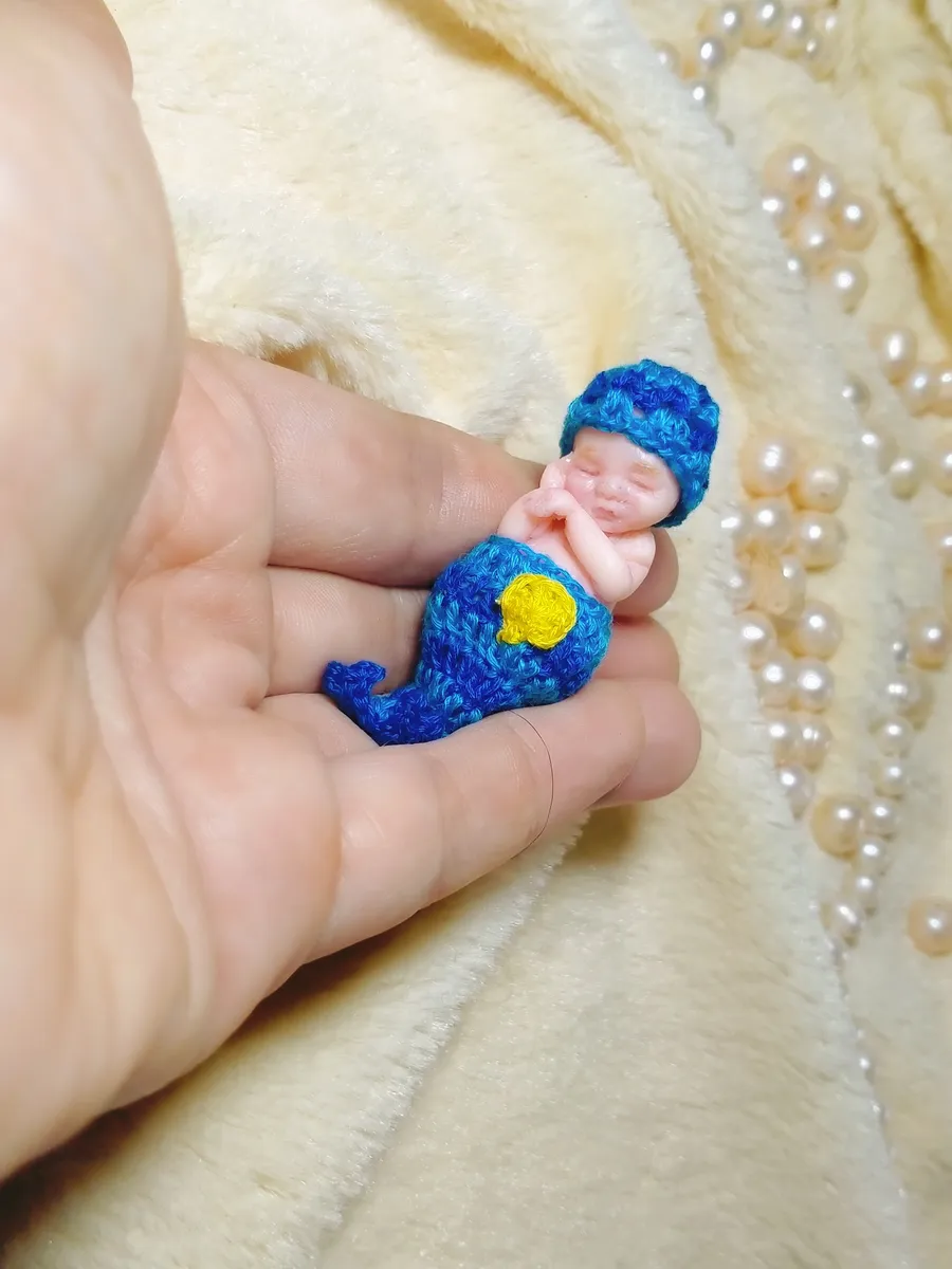 Whimsical OOAK miniature baby doll in blue crocheted crescent moon costume with yellow star, laying on cream blanket with pearl beads - by Mini Baby Dolls